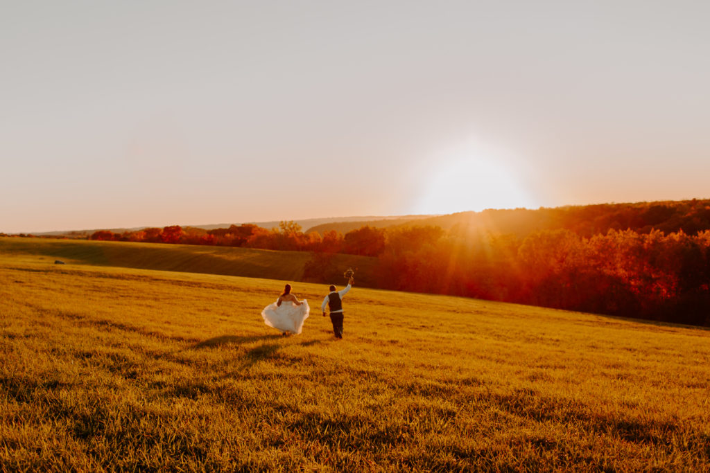 Couple running through a field outside La Crosse Wisconsin at sunset on their wedding day
